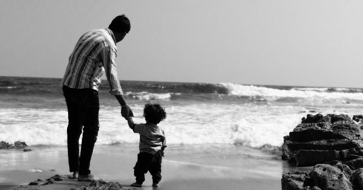 Father's helplessness in the poem shown through father and toddler walking on beach.